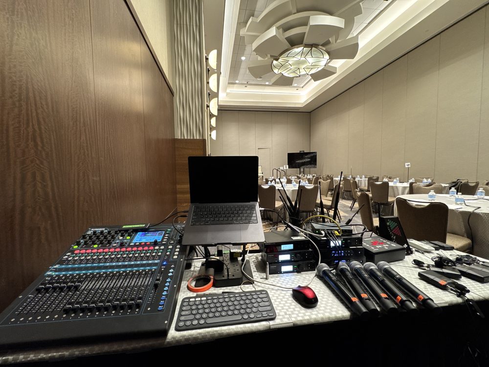 Elegant ballroom set for a banquet with round tables and a front-of-house audio setup in the foreground