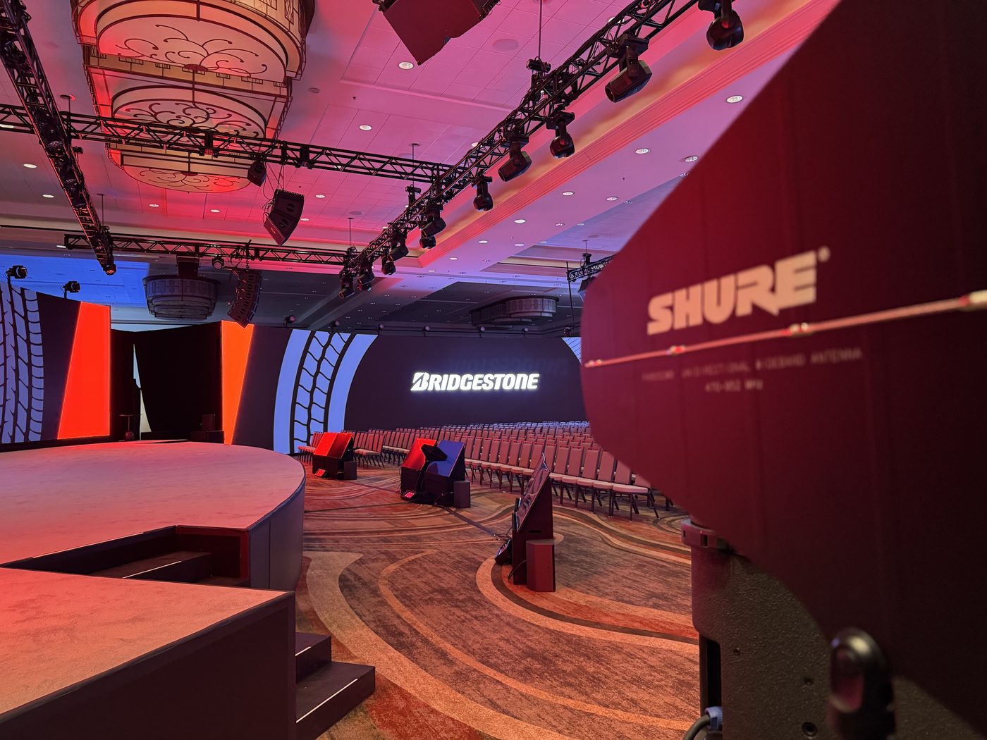 Curved LED video wall and stage lighting rig glowing pink and purple at a corporate keynote event