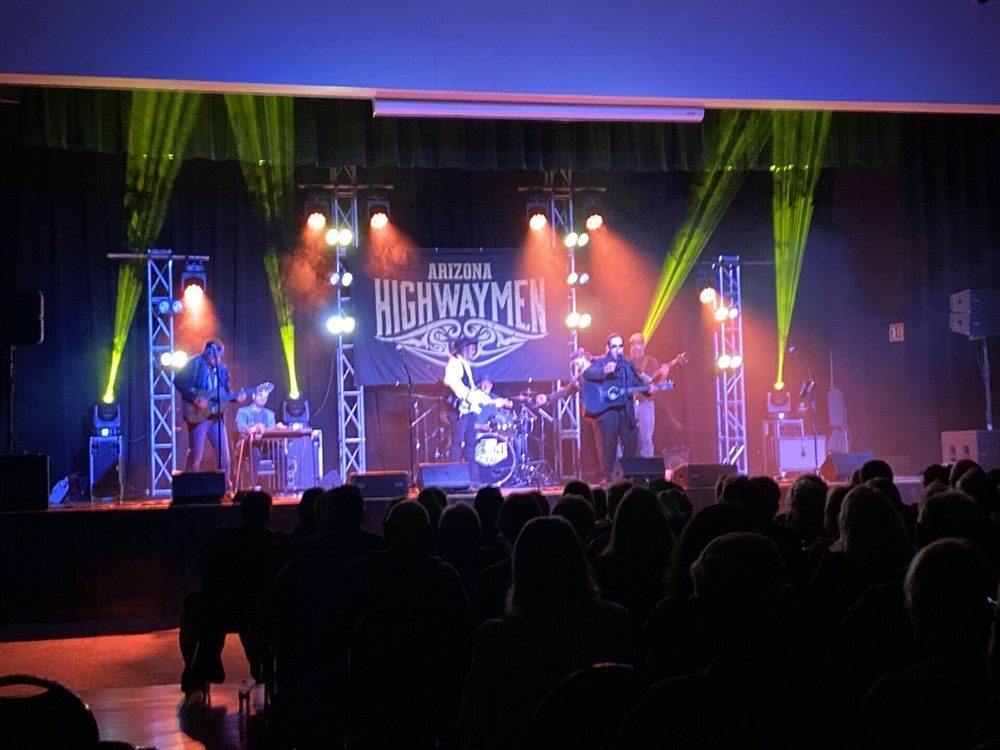Live band performing on stage under colorful concert lighting with crowd in front