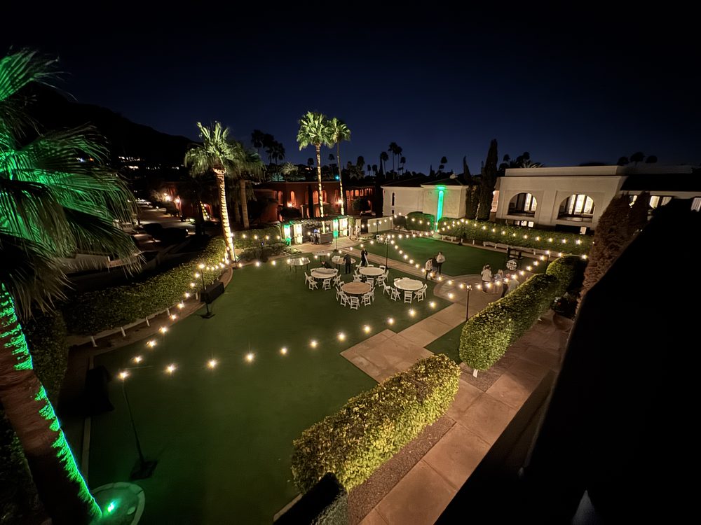 Outdoor evening reception at a desert resort venue with bistro string lights strung overhead and green uplighting on palm trees