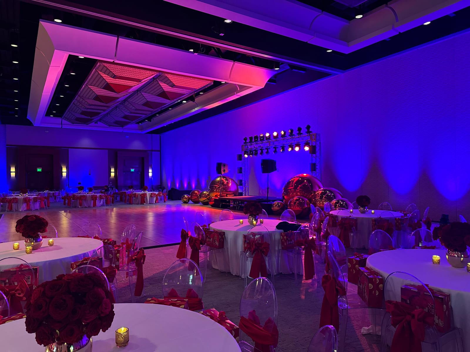 Elegant ballroom set for a gala with blue and purple uplighting, a lighting truss with moving heads, mirror ball décor, and round tables with red rose centerpieces